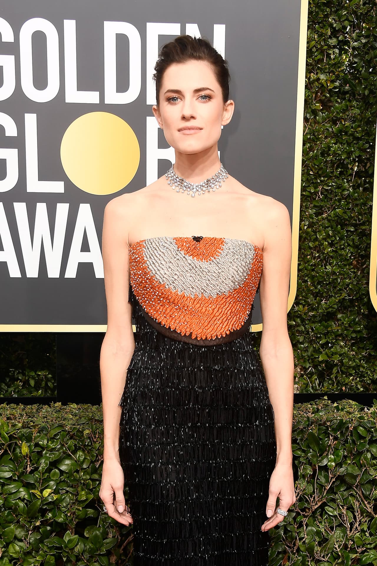 Allison Williams añade un toque de color con la pechera naranja y gris de su vestido negro de pedrería.