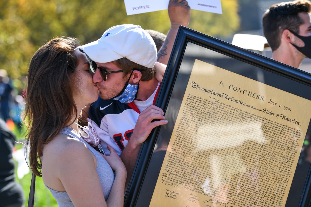 Una pareja celebra besándose mientras sostiene la Constitución de los EE. UU. durante la reunión de conteo de cada voto en Filadelfia en el Independence Hall.