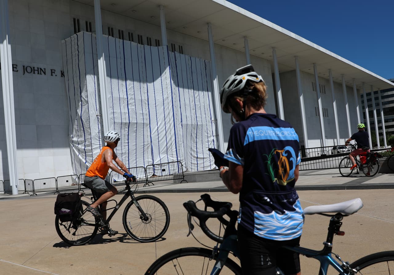 Ciclistas se detienen a observar la lona que cubre el letrero del Centro John F. Kennedy.