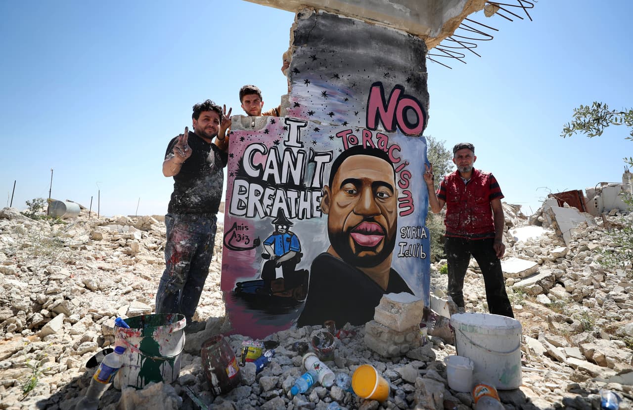 <b>Binnish, Siria.</b> Los artistas Aziz Asmar y Anis Hamdoun posan frente al mural de George Floyd que pintaron en las ruinas de una ciudad destruida por la guerra.