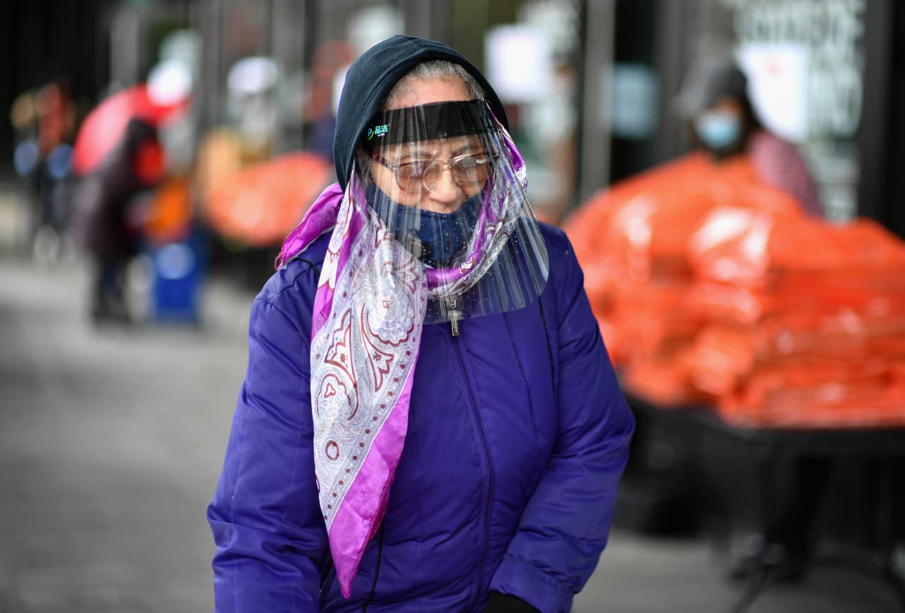 Una mujer usa un protector de plástico mientras espera en la fila del Banco de Alimentos en la plaza del Barclays Center