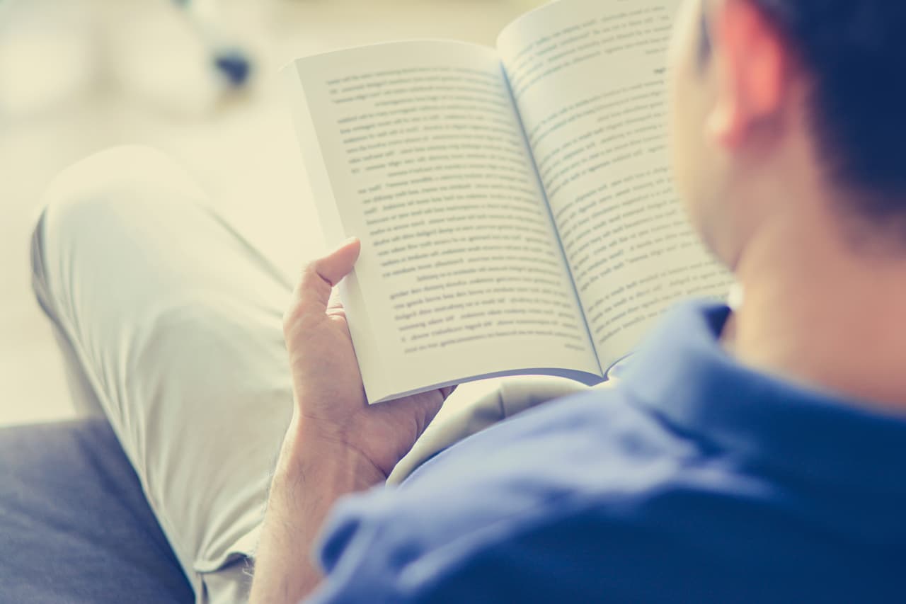 Young man reading book while sitting on the couch (over shoulder view) - vintage tone, soft focus