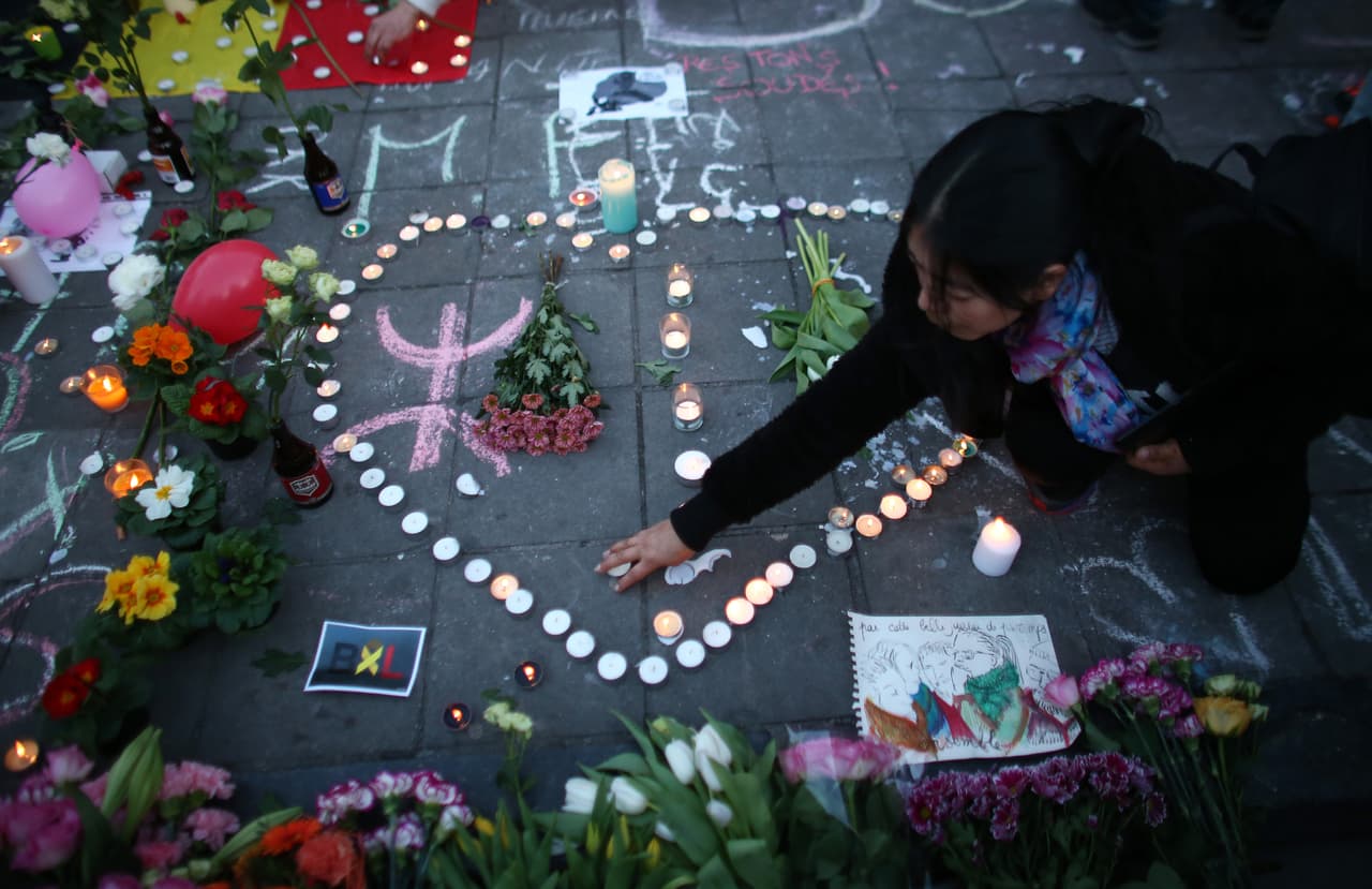 Una mujer enciende una vela mientras la gente se reúne para dejar tributos en Place de la Bourse.