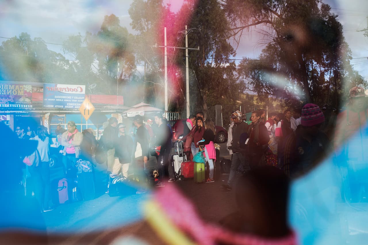 Ahora, muchos venezolanos que no tienen pasaporte se están viendo obligados a entrar de manera ilegal por trochas y caminos alternativos, con los riesgos que eso implica para su seguridad. En la imagen, un grupo de migrantes se refleja en un cartel de turismo de Colombia.