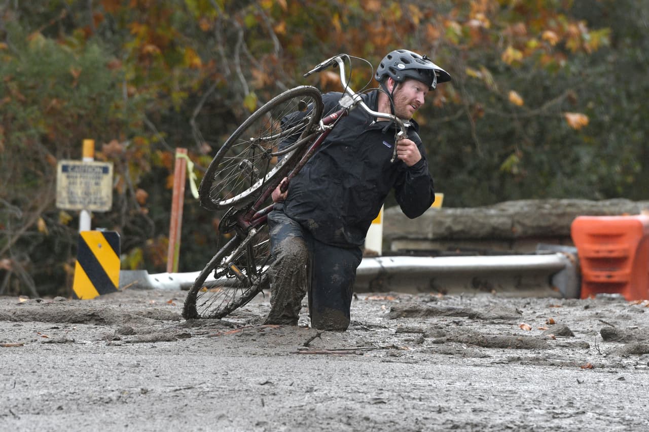 Jeff Gallup, residente de Carpinteria, California, carga su bicicleta mientras navega sobre el lodo que dejó la lluvia.