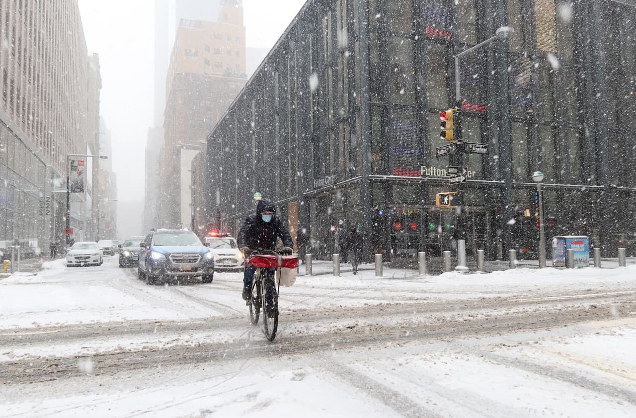 Un repartidor de restaurantes atraviesa Broadway en bicicleta durante la tormenta de nieve
