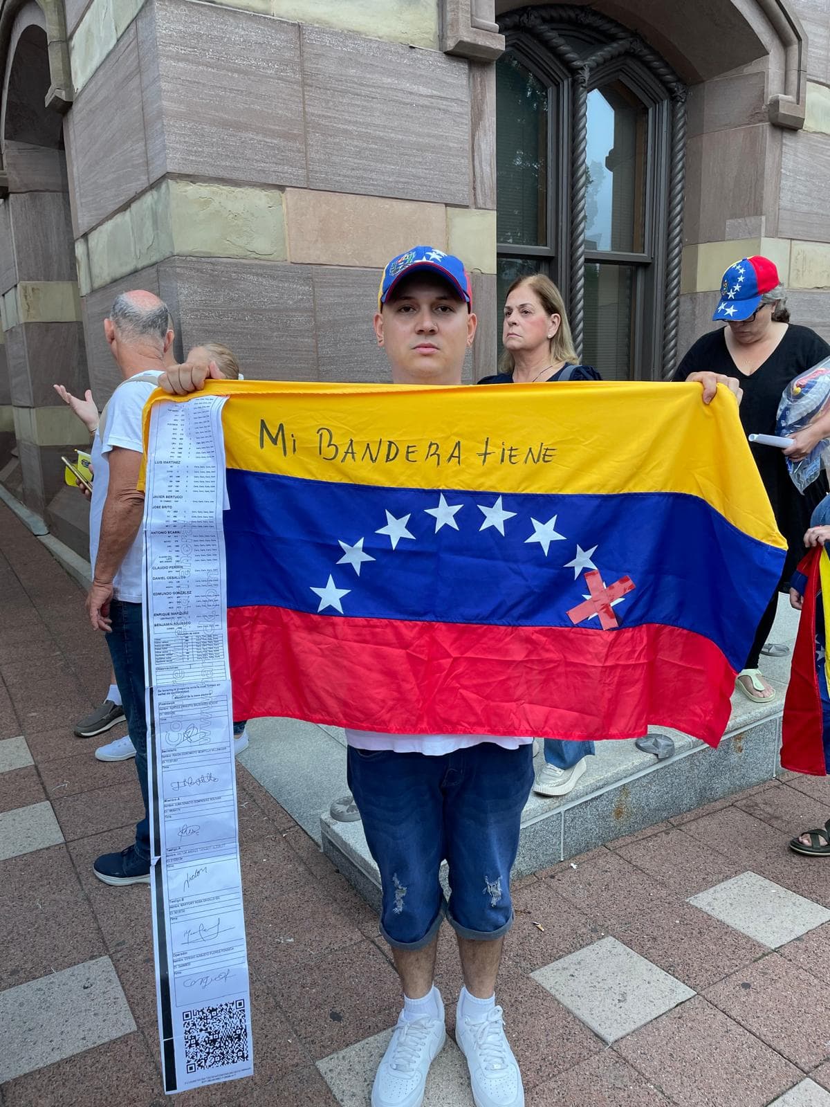 Un venezolano protesta con la copia de una de las actas en la mano y la bandera de siete estrellas, siete era el número de las provincias que firmaron el acta de la Independencia: Barcelona, Barinas, Caracas, Cumaná, Margarita, Mérida y Trujillo. El chavismo agregó una estrella