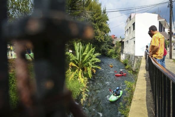 Los lugareños observan desde un puente mientras Juanito de Ugarte, Seth Ashworth y Rafael Ortiz reman por una quebrada poco profunda en el pueblo.