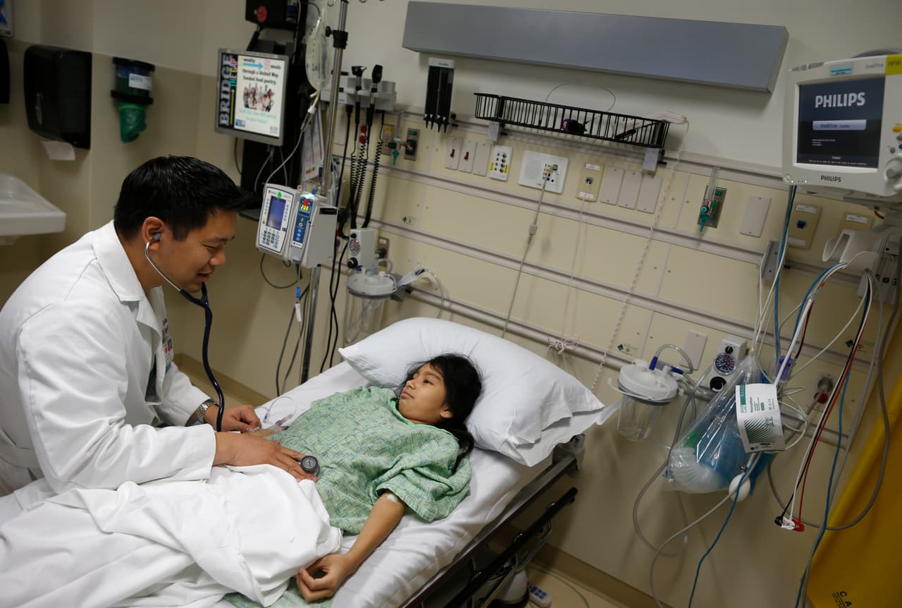 La paciente Analy Navarro es revisada por el doctor Leon Yeh en la sala de emergencias del Centro Médico Saint Francis en Peoria, Illinois, el 26 de noviembre de 2013. Un experimento en esa y otras ciudades buscaba transformar 
<b>la manera en que los médicos, las enfermeras y los hospitales prestan atención a los pacientes</b>, con el objetivo de reparar el sistema de salud, que es costoso y está plagado de errores. Los modelos de atención propuestos por la legislación tienen el objetivo de alentar a los proveedores a formar redes para coordinar la atención y reducir los costos, e implican una estrecha vigilancia de los pacientes más enfermos para tratar problemas de salud antes de que causen un costoso viaje a la sala de emergencias o una estancia hospitalaria prolongada.