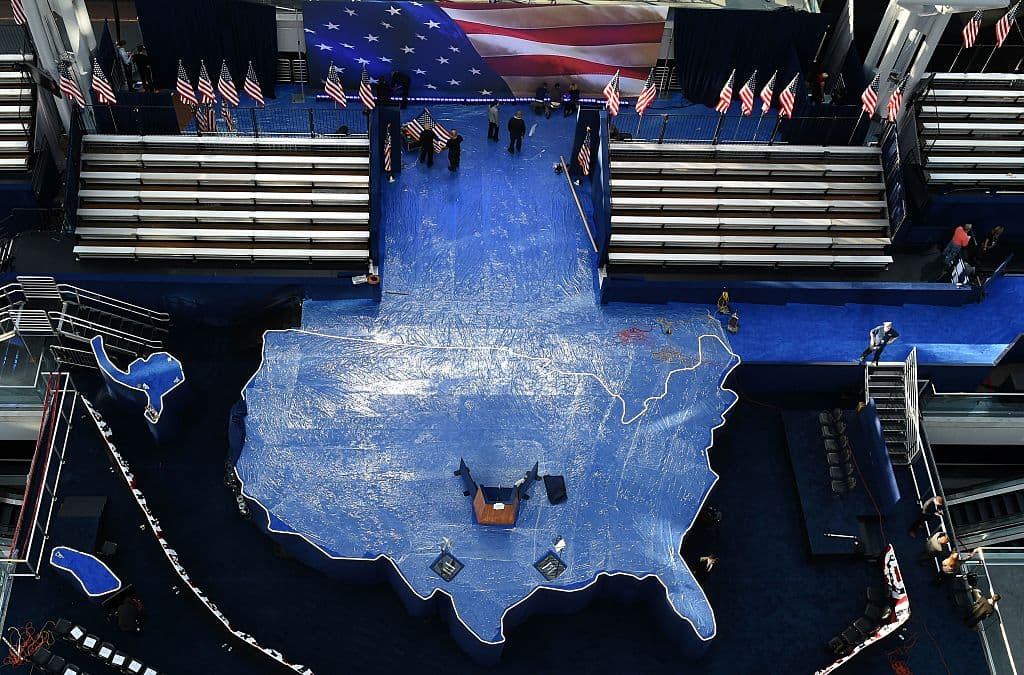 Trabajadores planchan la bandera de Estados Unidos mientras preparan un mapa que será el escenario del evento que recibirá a Hillary Clinton en el centro de convenciones Jacob K. Javits.