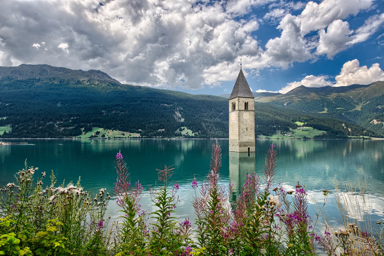 <b>Lago de Resia, Italia. </b>Ubicado en la frontera con Austria, es famoso por el campanario sumergido de una iglesia románica del siglo XIV. 
<a href="https://viaggi.corriere.it/itinerari-e-luoghi/lago-di-resia-curon-campanile-sommerso-alto-adige/" target="_blank">En 1950 se realizaron obras para una presa hidroeléctrica</a> que unió dos cuencas naturales. El agua sumergió al antiguo pueblo, Curon Venosta, y los habitantes vivieron una migración forzada que los llevó a levantar el nuevo Curon Venosta. El lugar luce como un escenario para un cuento de hadas, con la torre en medio del espejo de agua cristalina, rodeado de montañas. En invierno, cuando el lago se congela se puede caminar hasta el campanario.
<br>