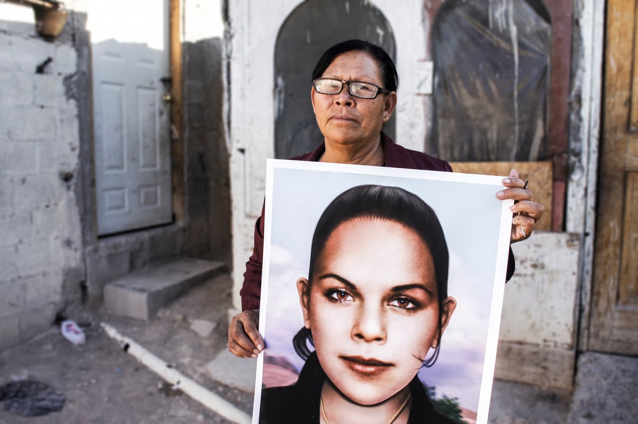 Julia Calderas holds a portrait of her daughter Maria Elena, one of the hundreds of women who disappared during a wave of murders of women in Ciudad Juárez. Calderas helped paint the fence. Photo: Estephani Cano.
