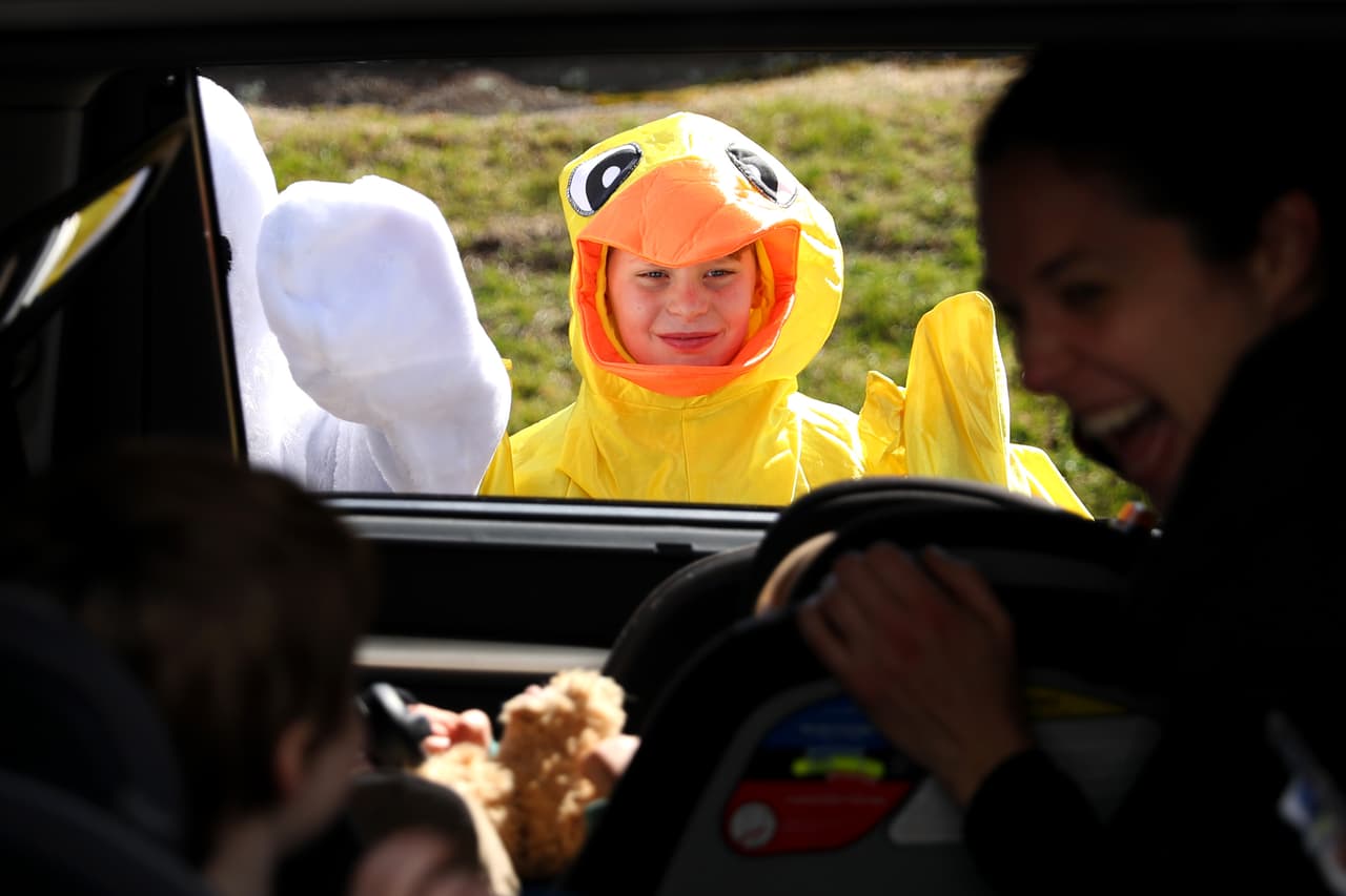 <b>Celebración de la Pascua en la pandemia</b>. Dos niños disfrazados saludan a los asistentes a un servicio religioso en sus autos en Newton, Massachusetts, el 11 de abril. En todo el país pastores y sacerdotes han continuado los servicios religiosos con este sistema desde el inicio de las regulaciones.