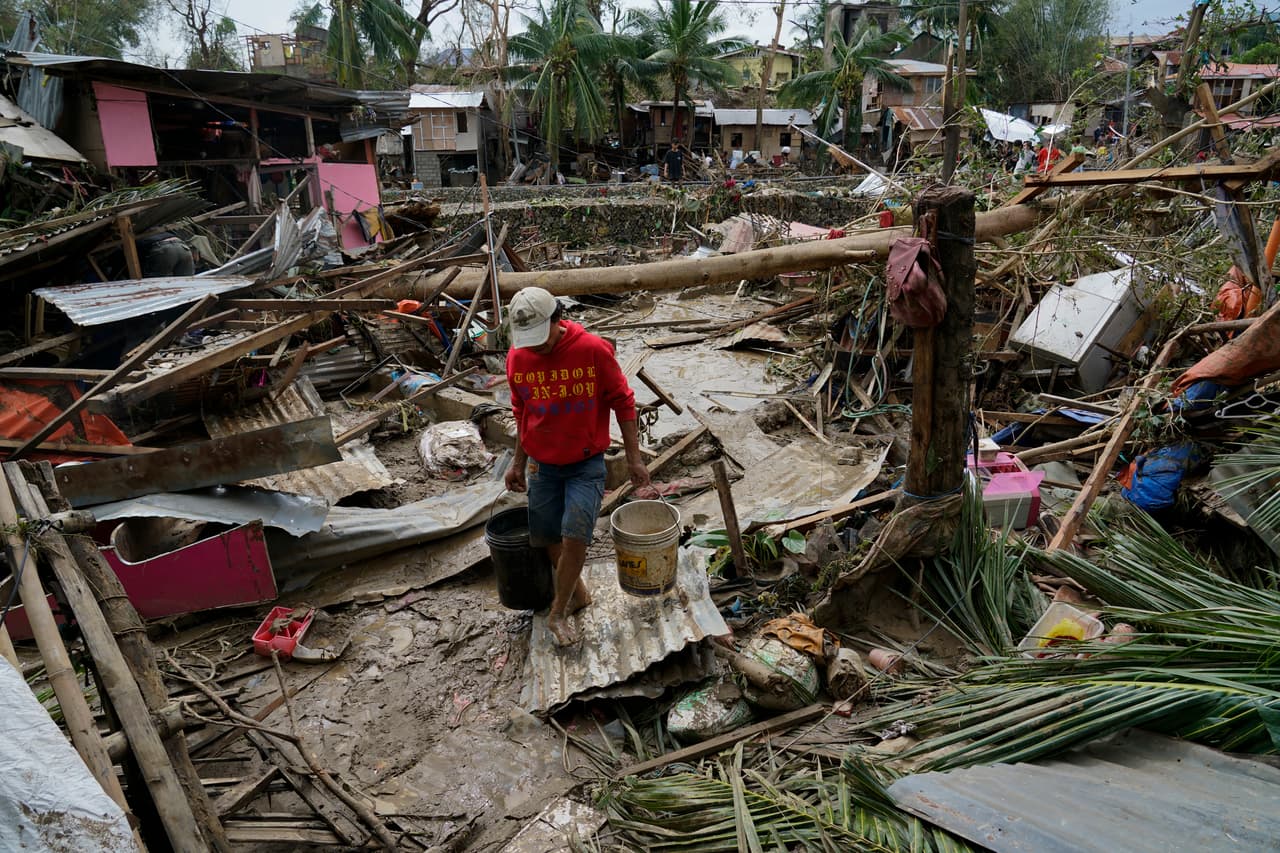 Un hombre carga cubos junto a casas dañadas por el tifón Rai en Talisay, en la provincia de Cebú, Filipinas, el pasado viernes 17 de diciembre de 2021.