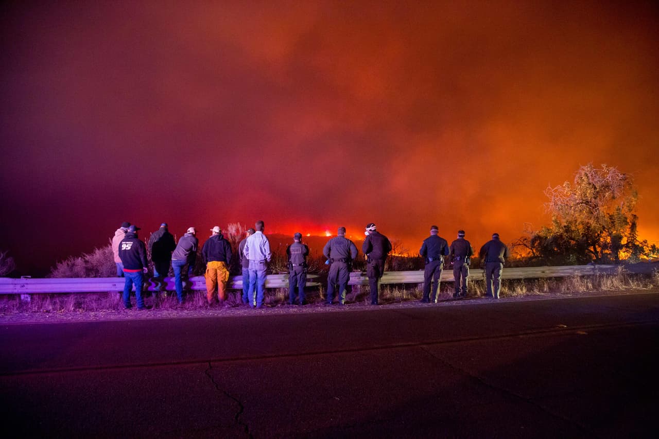 Equipos de policías y bomberos observan mientras el fuego Thomas quema una ladera en Ojai, California.