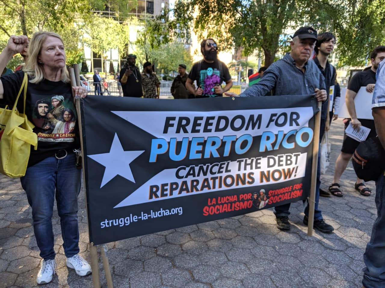 Una pancarta dice: "Libertad para Puerto Rico, Cancelen la deuda, ¡reparaciones ahora!"