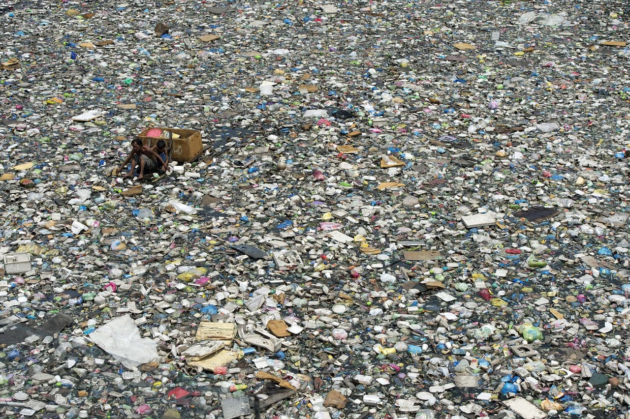 Entre 4.8 y 12.7 millones de toneladas de plásticos van a parar a ríos y océanos cada año, según la Universidad de Georgia (EEUU). Esta es una barca improvisada en la cual un padre y su hijo navegan a través de un río contaminado en Manila, Filipinas. Allí recogen botellas de plástico que pueden vender para reciclaje. Ganan unos tres dólares al día. (Foto de marzo de 2015).