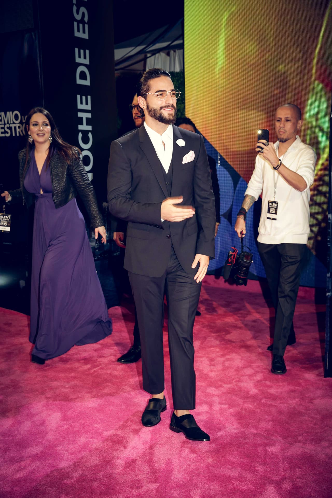 Maluma no podía fallar al vestir completamente de los diseñadores italianos Dolce & Gabanna con un traje negro slim fit con pañuelo y flor blanca en la solapa perfectamente combinados con unos slippers de terciopelo.
