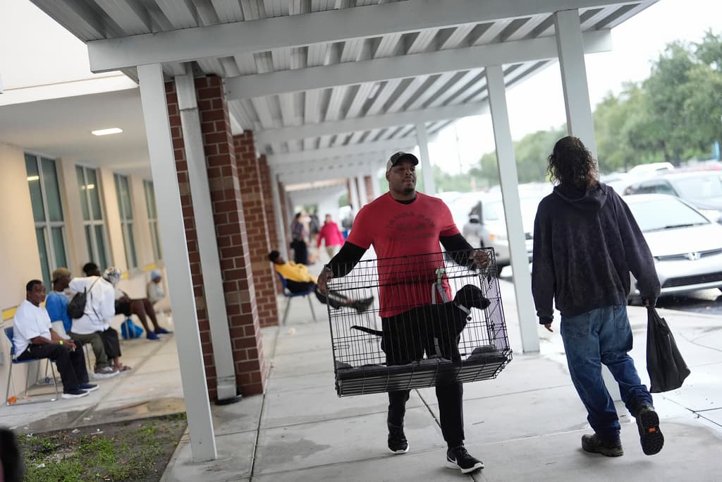<b>Se va con su mejor amigo: </b>Un hombre lleva un perro en una jaula a la escuela secundaria Gibbs, un refugio del gobierno donde 1,700 personas ya habían buscado refugio a última hora de la mañana del miércoles 9 de octubre de 2024, antes de la llegada del huracán Milton a San Petersburgo, Florida.