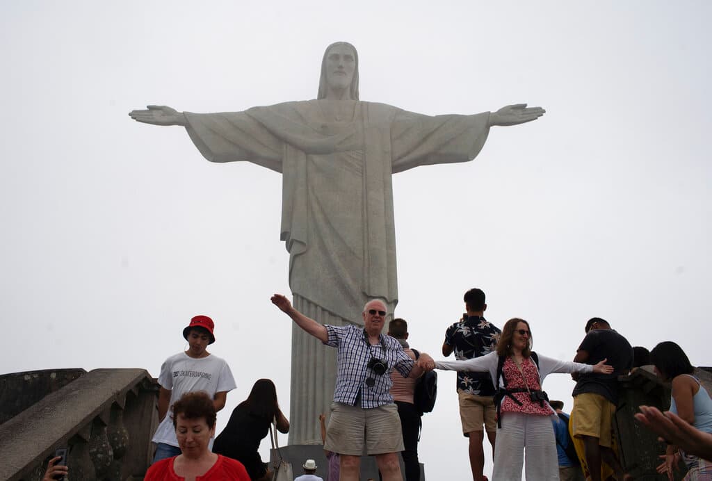 Turistas posan para la foto frente a la estatua de Cristo Redentor durante un día con neblina en Río de Janeiro, Brasil, el martes 17 de marzo de 2020.