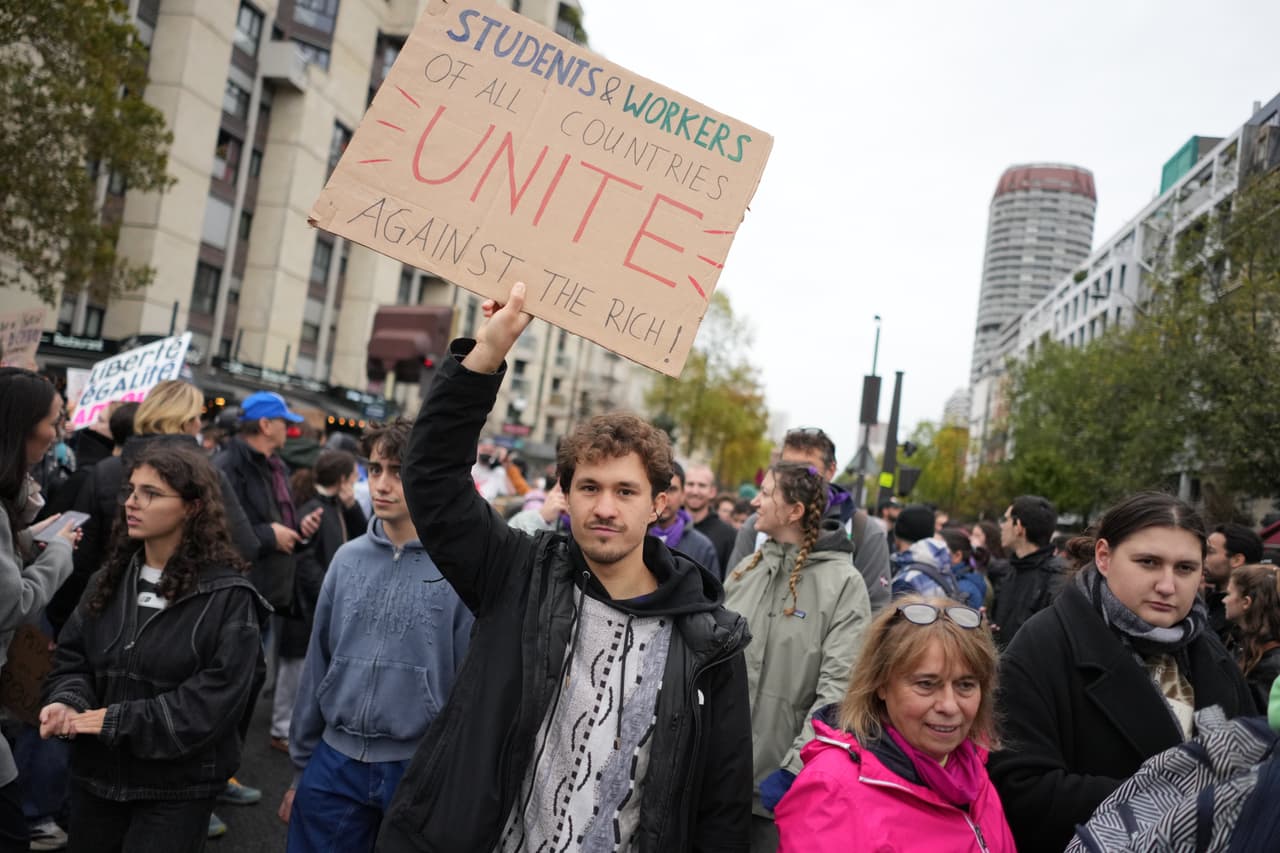 Otro protestante sostiene un rótulo que señala: "Estudiantes y trabajadores de todos los países, unanse contra los ricos".