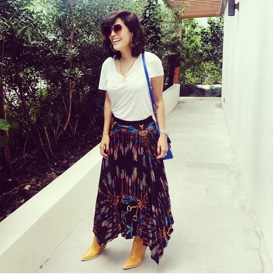 Vemos a Karla Martínez con un estilo muy casual donde resaltan dos prendas: las botas en color amarillo opaco con la falda estampada larga en corte asimétrico y la bolsa de tirante largo. El azul que lleva en el bolso también forma parte de la gama de colores tropicales.