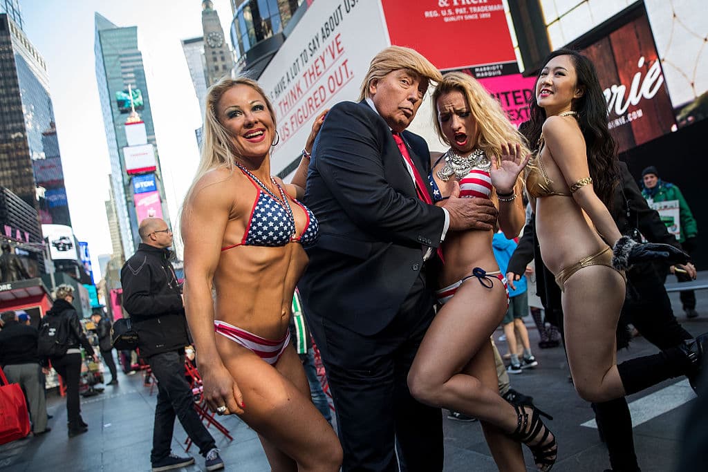 NEW YORK, NY - OCTOBER 25: (EDITOR'S NOTE: Image contains profanity.) A Donald Trump look-a-like gestures as he poses with bikini-clad women in Times Square, October 25, 2016 in New York City. The stunt was organized by artist Alison Jackson. (Photo by Drew Angerer/Getty Images)
