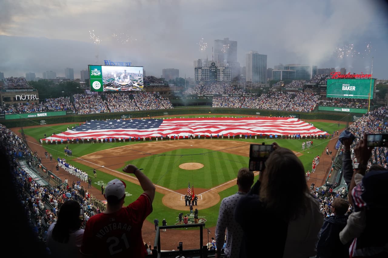La gente se pone de pie para escuchar el himno nacional antes de un partido de béisbol entre los Cachorros de Chicago y los Cardenales de San Luis, el sábado 4 de julio de 2026, en Chicago.