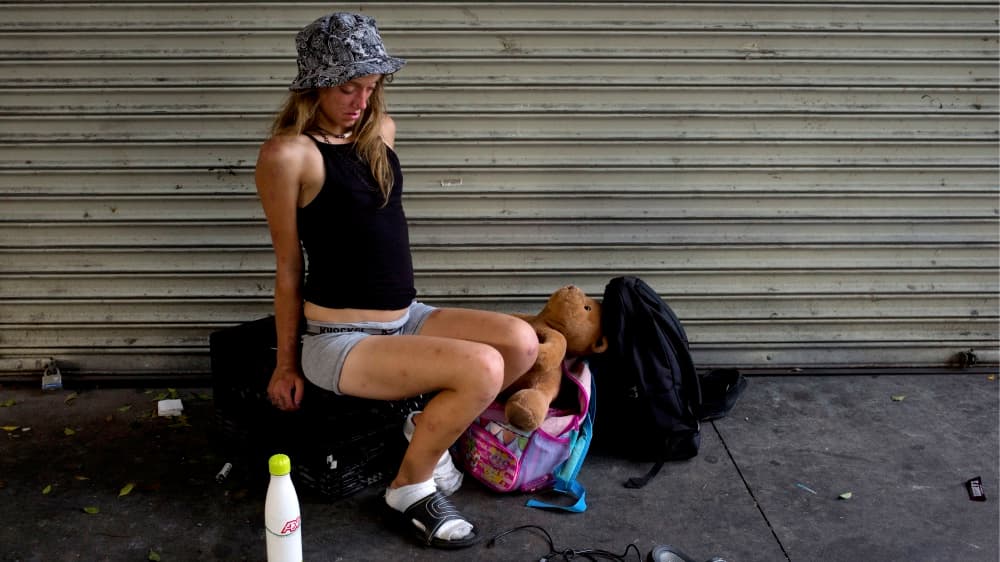 Una joven mujer que vive en las calles de Skid Row se tambalea sobre una caja luego de haberse inyectado una dósis de heroína.