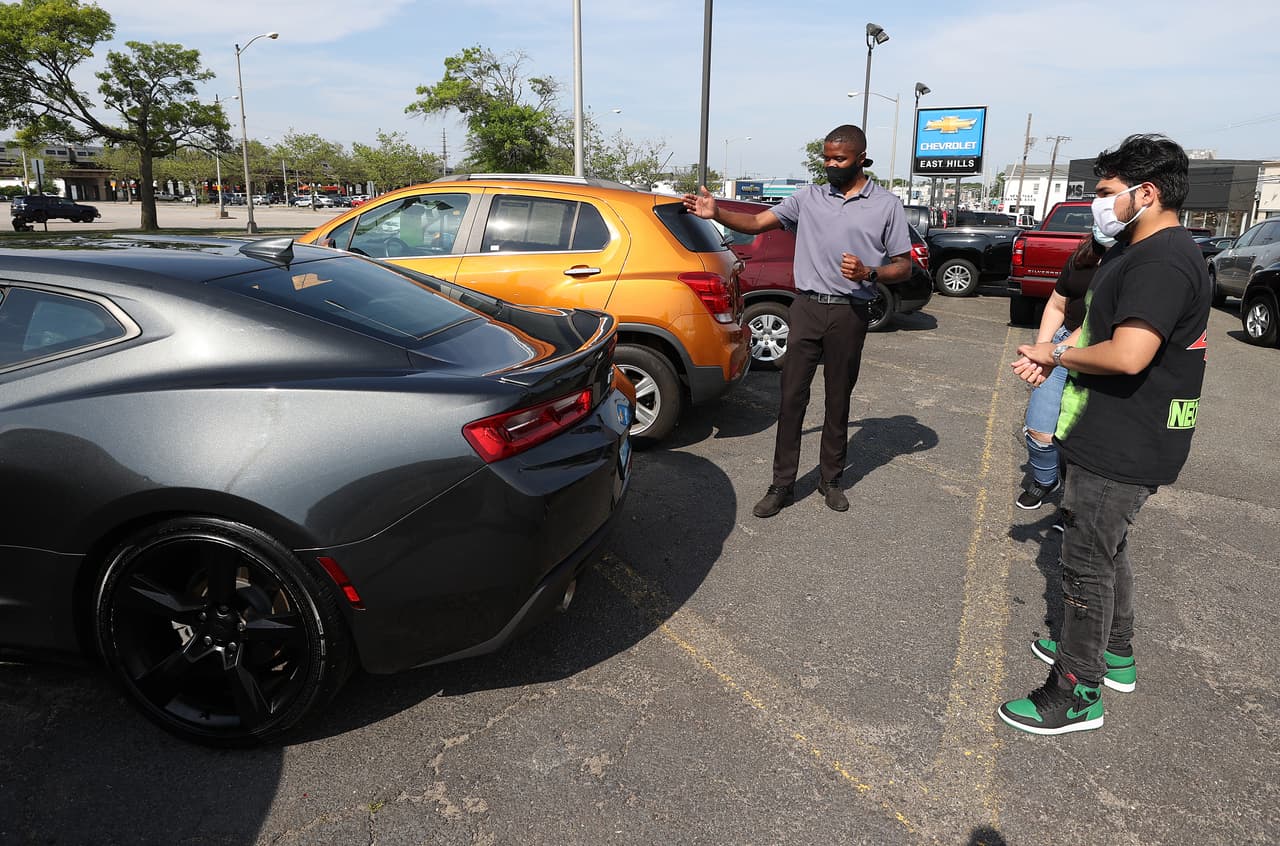 Cheyen Shilletto habla con sus clientes Julio Larrea y Satima Cruz en el estacionamiento del East Hills Chevrolet en Freeport, Nueva York. Los concesionarios de coches también fueron autorizados a reabrir como parte de la Fase II.