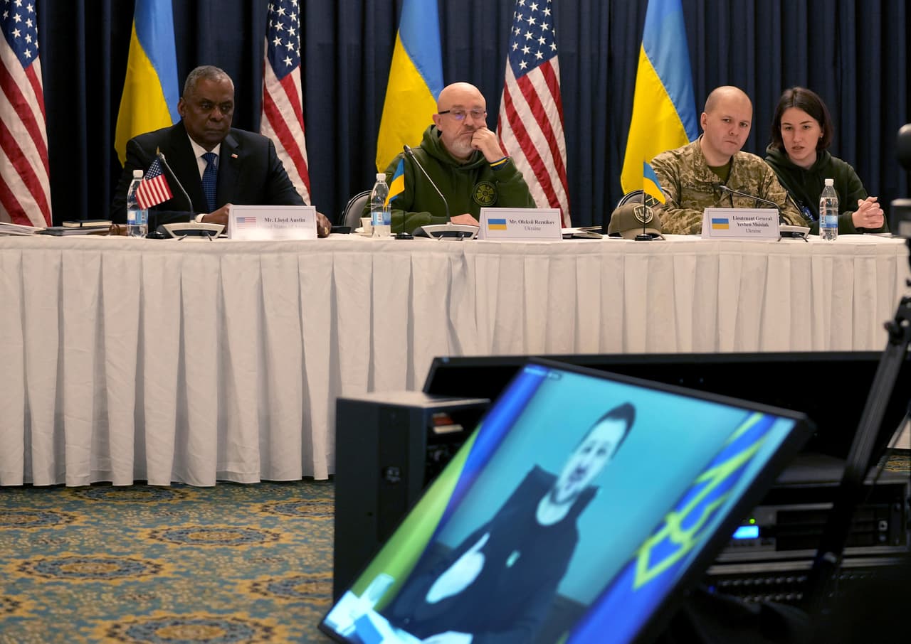 El secretario de Defensa de Estados Unidos, Lloyd Austin, en la parte trasera izquierda, escucha el discurso del presidente de Ucrania, Volodymyr Zelenskyy, (en una pantalla de video) durante la reunión del "Grupo de contacto de defensa de Ucrania" en la base aérea de Ramstein en Ramstein, Alemania.