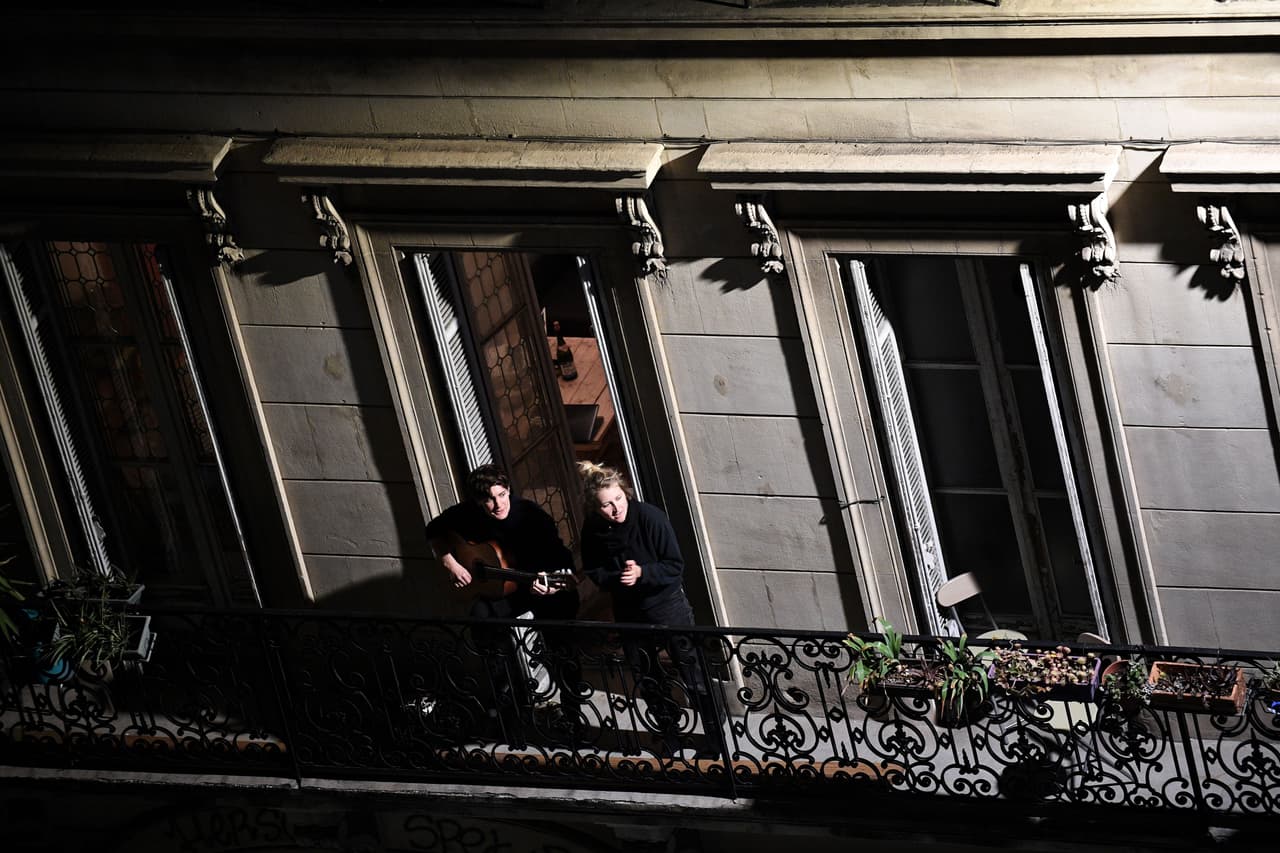 Dos mujeres, una toca la guitarra y la otra aplaude, desde su balcón a los empleados de salud en Marsella.