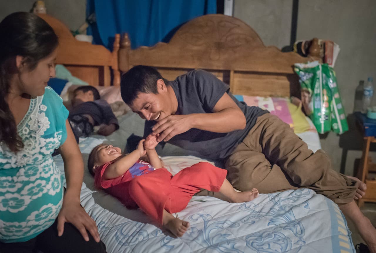 Mientras duerme Leandro, Santiago García hace cosquillas Josué antes de acostarse en la habitación compartida de la familia en Santa Ana. Santiago García construyó la casa de su familia en la misma parcela de tierra de sus padres y tiene la intención de continuar en esta casa para el resto de su vida.