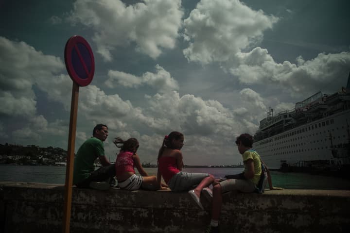 En la Avenida del Puerto, tres niños y un adulto observan los cruceros que llegan a La Habana.