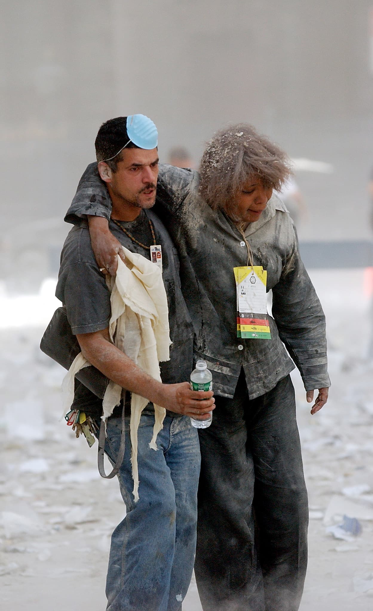 Un hombre asistiendo a una mujer a salir de la zona del World Trade Center, la que desde ese momento empezará a conocerse usando el lenguaje bélico como Ground Zero (o Zona Cero), que es el punto donde estalla un bomba antes de llegar a la superficie.