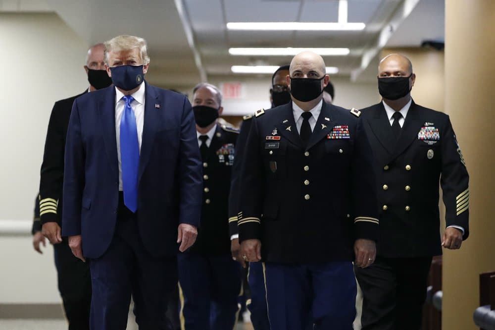 El presidente 
<a href="https://www.univision.com/temas/donald-trump">Donald Trump</a>, en primer plano a la izquierda, usa una máscara 
<b>mientras camina con otros por un pasillo durante una visita al Centro Médico Militar Nacional Walter Reed en Bethesda, Maryland</b>, el 11 de julio de 2020.