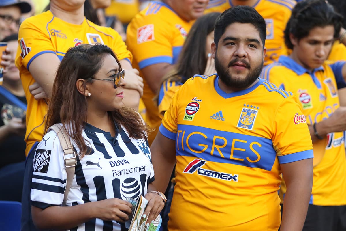 Una pareja comparte en el Estadio Universitario, ella de Rayados y él de Tigres.