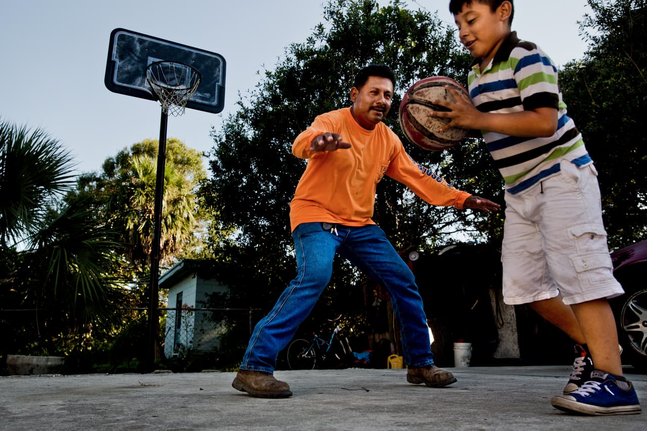 Juvenal Dominguez, 42, plays basketball with his son Alan outside of their home in Vero Beach, FL on Wednesday, July 5, 2017. Soon after they began playing, Dominguez's injured knee began acting up and he had to stop playing with his son. (Photo by Scott McIntyre for ProPublica)