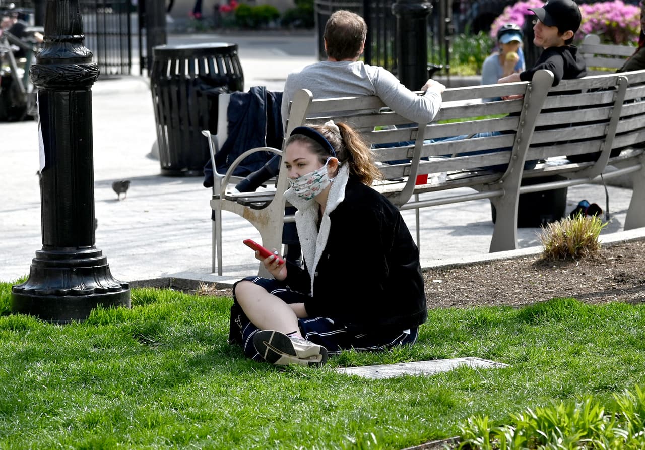 Una mujer lleva una máscara de tela con un patrón floreado mientras disfruta del sol en el parque