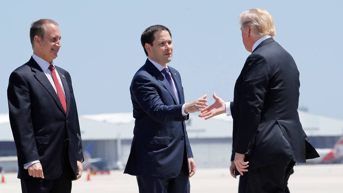 El senador Marco Rubio saluda al presidente Trump, mientras el Representante Mario Díaz-Balart, Republicano de Florida, los observa en el Aeropuerto Internacional de Miami, el lunes 16 de abril de 2018.