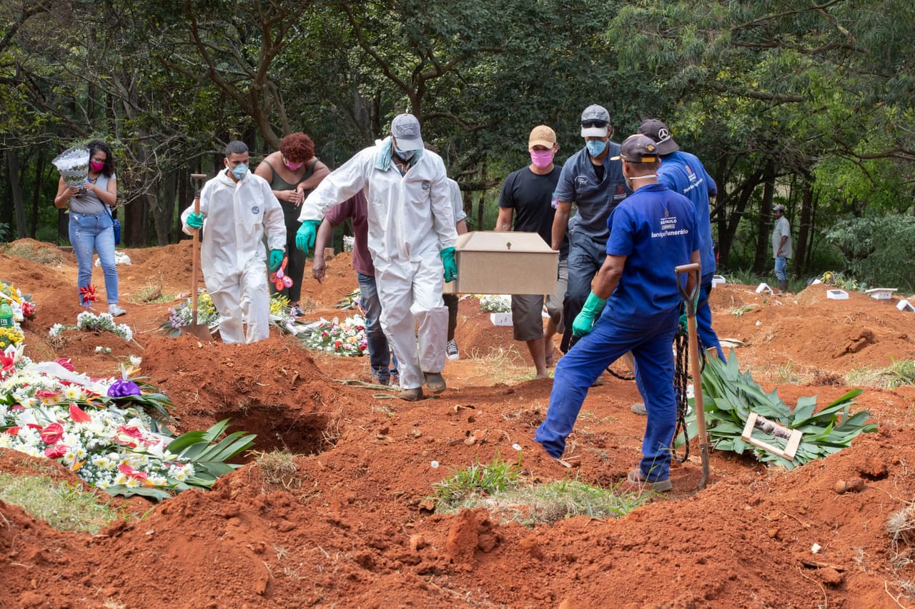 Trabajadores de un cementerio, protegidos con trajes especiales, cargan el ataúd con los restos de una personas que falleció por coronavirus en Sao Paulo.