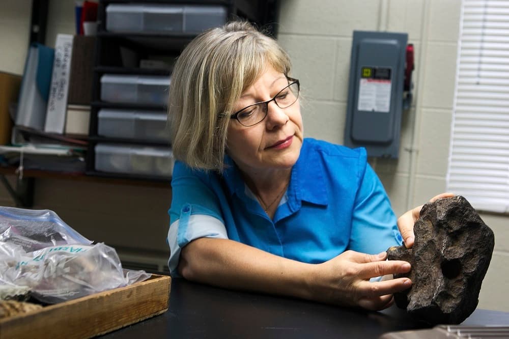 In this Sept. 14, 2018 photo provided by Central Michigan University, Monaliza Sirbescu, a geology faculty member in earth and atmospheric sciences shows off a 22-plus pound meteorite that was being used as a doorstop on a farm in Edmore, Mich. The iron and nickel meteorite is the sixth largest meteorite found in Michigan, according to the Smithsonian Museum and Central Michigan University. Owner David Mazurek said the meteorite came with a barn he bought in 1988 in Edmore. He says the farmer who sold him the property told him it landed in his backyard in the 1930s. (Mackenzie Brockman/Central Michigan University via AP)