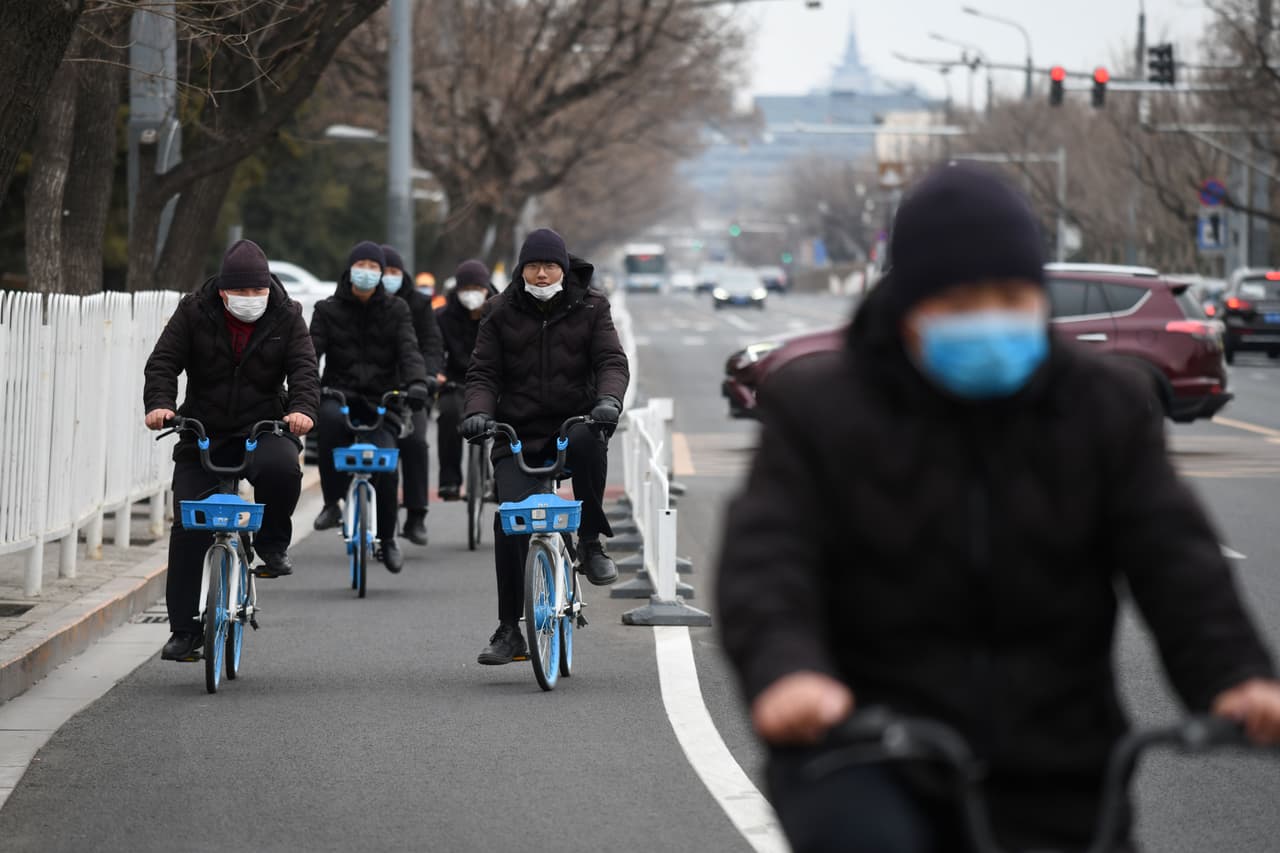 Gente con mascarillas se desplaza en bicicletas por una calle de Pekín.