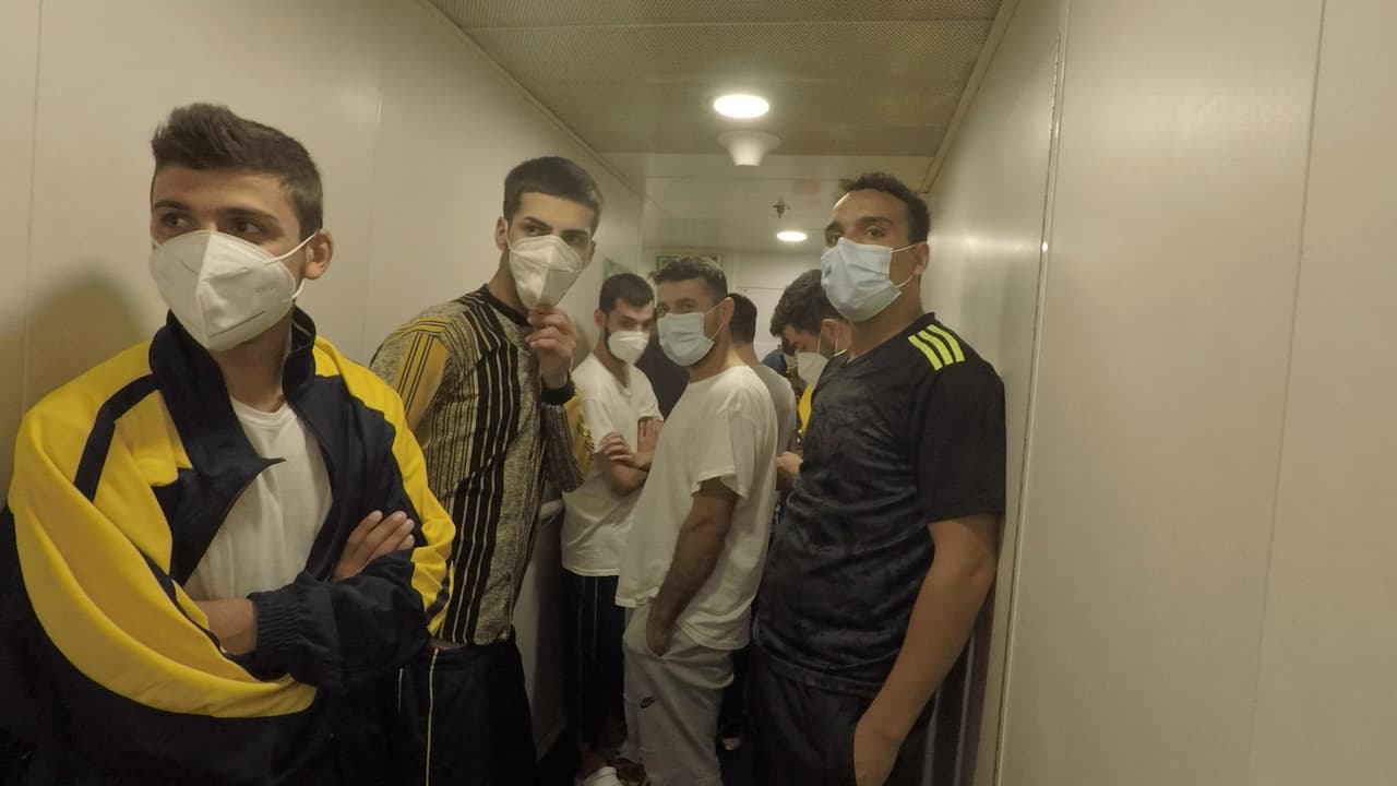 Migrantes enmascarados esperan en los pasillos