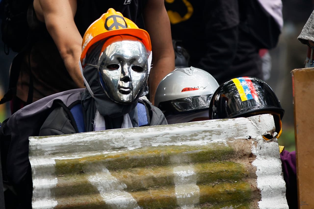 Masked demonstrators take cover during clashes with security forces at an opposition May Day march in Caracas, Venezuela, Monday, May 1, 2017. Venezuelans are taking to the streets in dueling anti- and pro-government May Day demonstrations as an intensifying protest movement enters its second month.