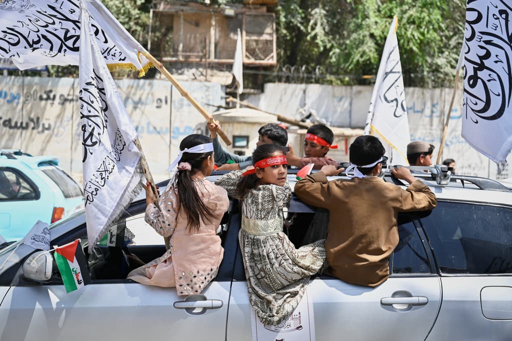 Unos niños viajan en un vehículo y ondean banderas talibanes.