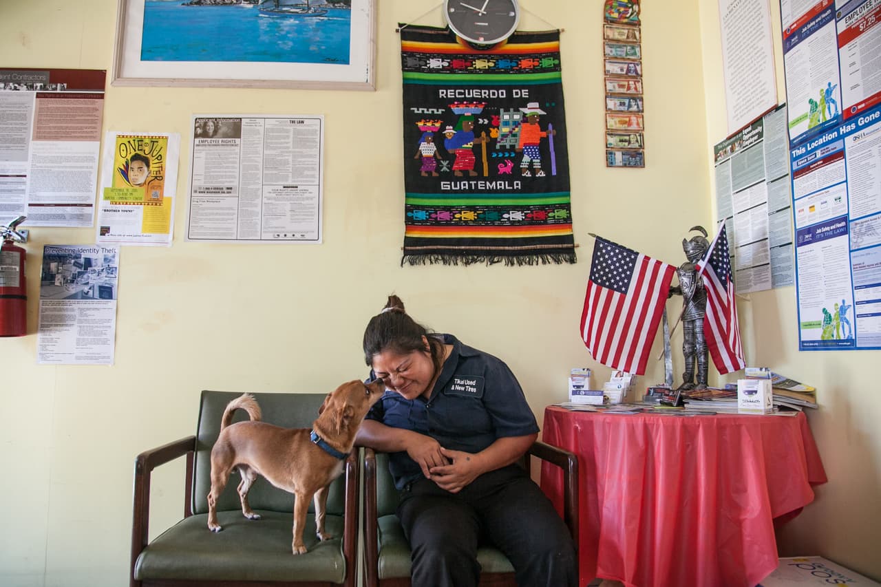 Víctor y Maty se conocieron años después en Providence (Rhode Island) a donde él fue a buscar mejores condiciones de trabajo y el primer destino de ella en EEUU. Maty fue invitada a una iglesia a la que iba un hermano de Víctor. "Él me contó que tenía sus hermanos y que si un día nos poníamos de acuerdo para cocinar algo y yo le conté que me gustaba cocinar mucho, pero que también cortaba pelo porque yo estudié belleza en Guatemala y me dijo a ver cuándo nos corta el cabello a mis hermanos". En la foto, Maty en la recepción del taller con el perro de la familia, Sparky.
<br>