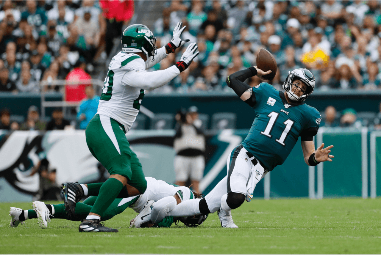 Carson Wentz de Philadelphia Eagles pasa el balón mientras es tacleado por Darry Roberts de los New York Jets, mientras Jordan Willis defiende.