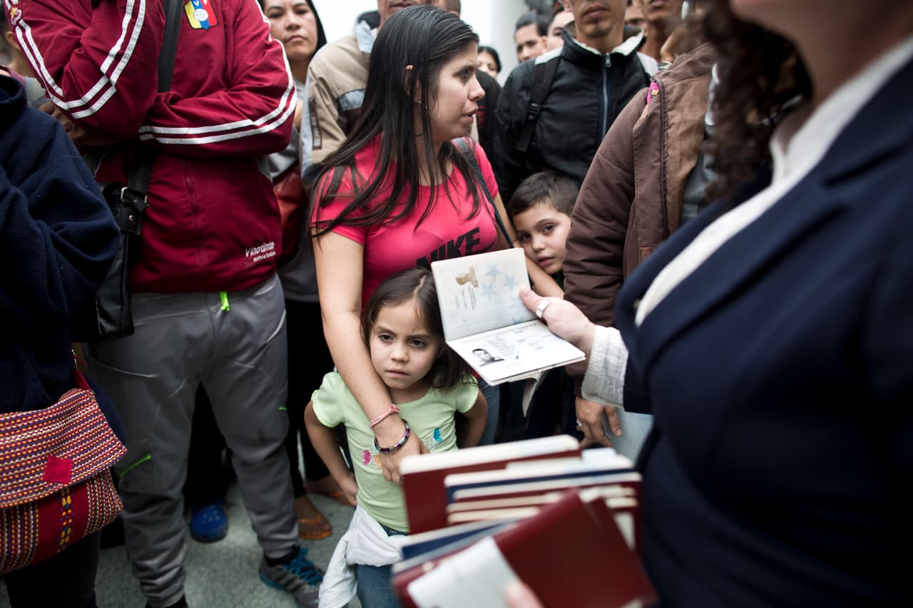 La medida entró en vigor mientras decenas de venezolanos estaban en tránsito por Colombia, por lo que se enteraron de su existencia al llegar al punto de migración. En la imagen, una funcionaria de reparte los pasaportes sellados a un grupo de migrantes.
