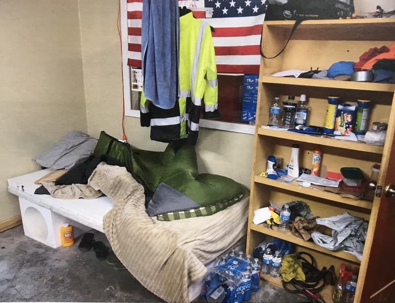 Una bandera estadounidense cuelga en la pared del “cuarto” de un trabajador, quien dormía sobre dos tablas y una colchoneta.